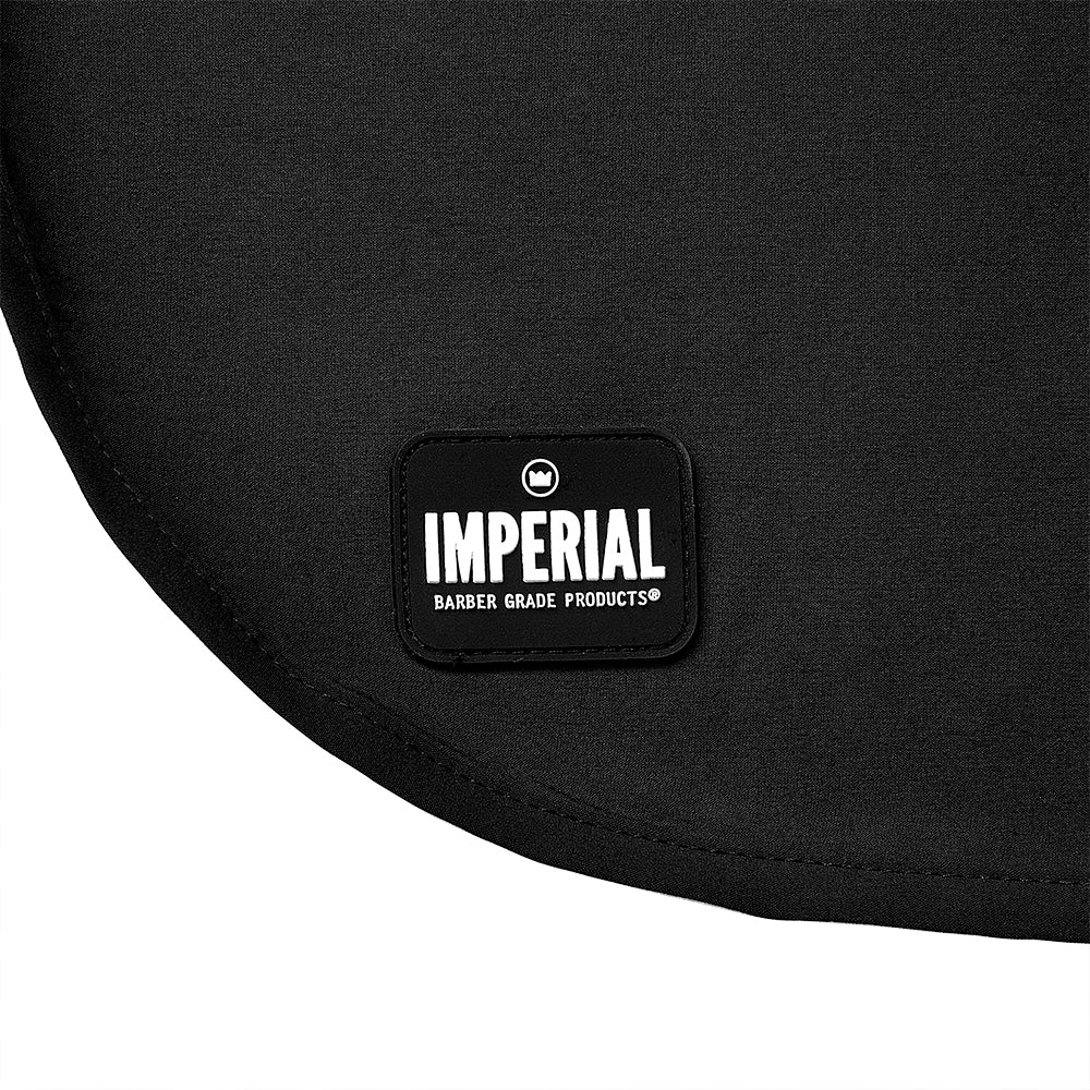 Close-up of the rubber Imperial Barber Grade Products badge stitched onto the lower front of the black Standard Edition barber cape.