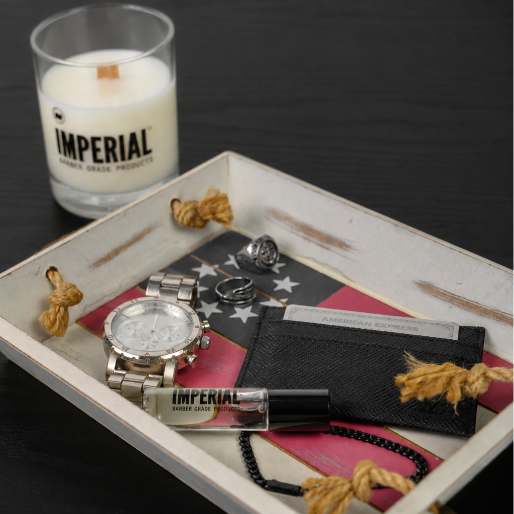 Imperial Crown One cologne travel vial and Imperial-branded candle styled on a valet tray with a watch, card wallet, and rings.