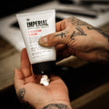 Tattooed hands squeezing a small amount of Imperial Freeform Cream from its 4 oz tube into an open palm.