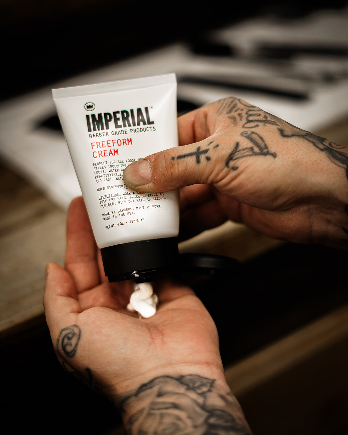 Tattooed hands squeezing a small amount of Imperial Freeform Cream from its 4 oz tube into an open palm.