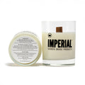Imperial Barber Grade Products scented candle in a clear glass with a wood wick, shown alongside its lid displaying warning and ingredient information.