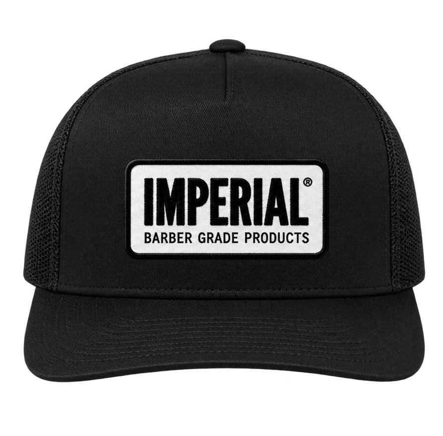 Front view of a black Imperial Barber Grade Products trucker hat with a rectangular woven patch bearing the Imperial Barber Grade Products logo in black on white.