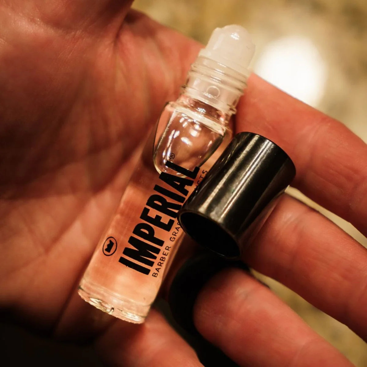 Close-up of a hand holding the uncapped Imperial Crown Roll cologne roller bottle, showing the ball applicator tip.