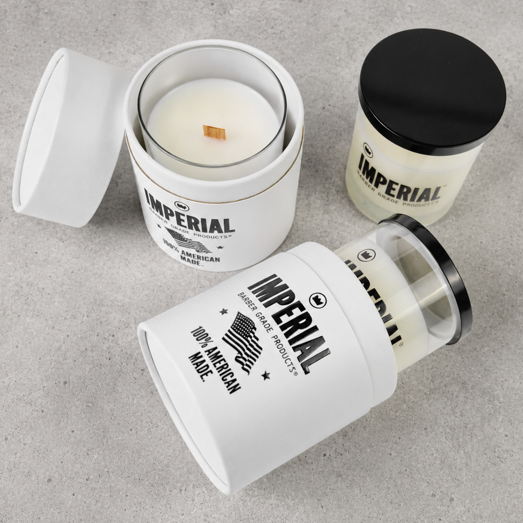 Three Imperial Barber Grade Products Standard Candles on a concrete surface, one open showing the wood wick, one capped in black, and one tipped on its side showing the 100% American Made label.